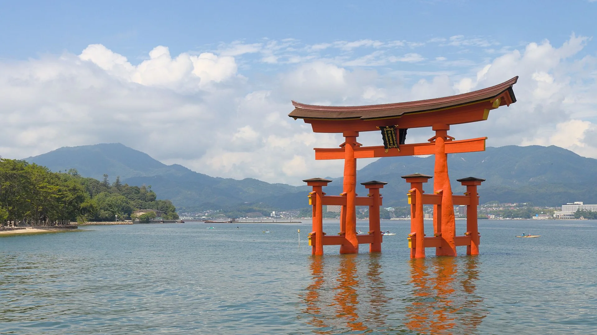The vermilion torii gate of Itsukushima Shrine standing in the sea off Miyajima, with the mountains of the Seto Inland Sea behind it