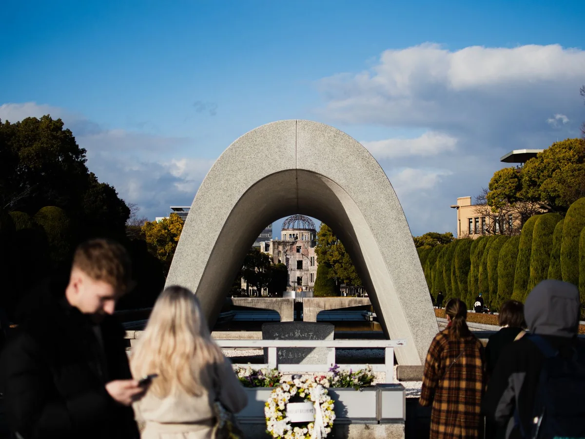 Visitors at the Memorial Cenotaph in Hiroshima Peace Memorial Park, with the A-Bomb Dome visible through the arch